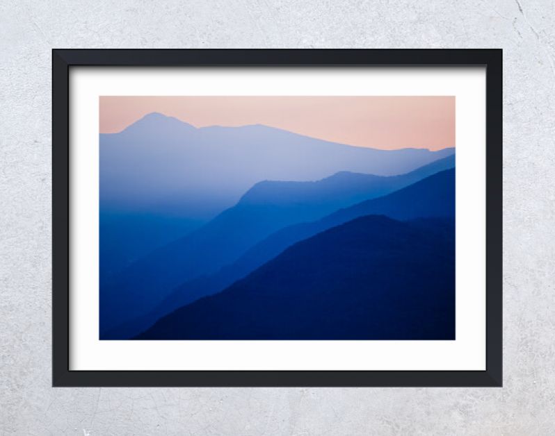 Stacked silhouettes of blue mountains underneath an orange evening sky at Lago Maggiore, Italy close to Switzerland. Original image with minimalist appearance. Ideal background with large copy space.