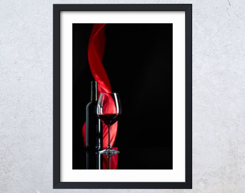 Wineglass and bottle of red wine on a black reflective background.