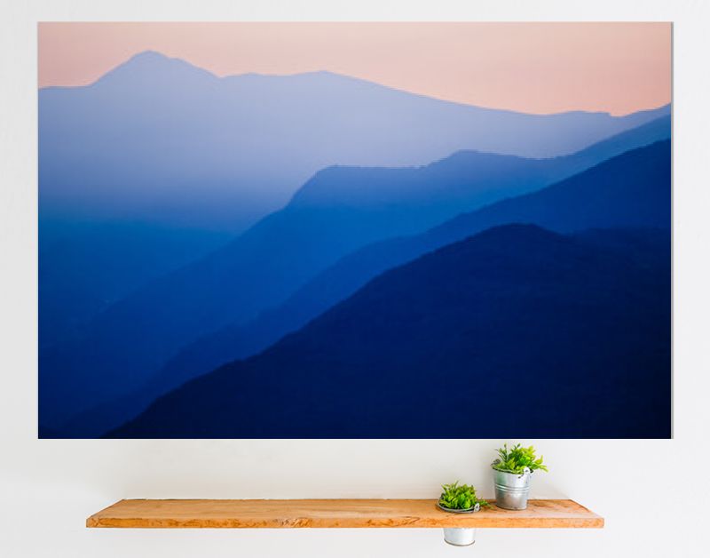 Stacked silhouettes of blue mountains underneath an orange evening sky at Lago Maggiore, Italy close to Switzerland. Original image with minimalist appearance. Ideal background with large copy space.